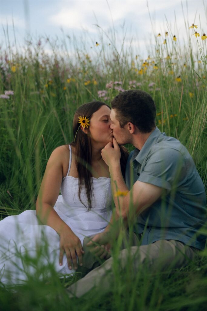 The couple kissing in a field of yellow and purple wildflowers, Sophie’s flower tucked behind her ear catching the light.