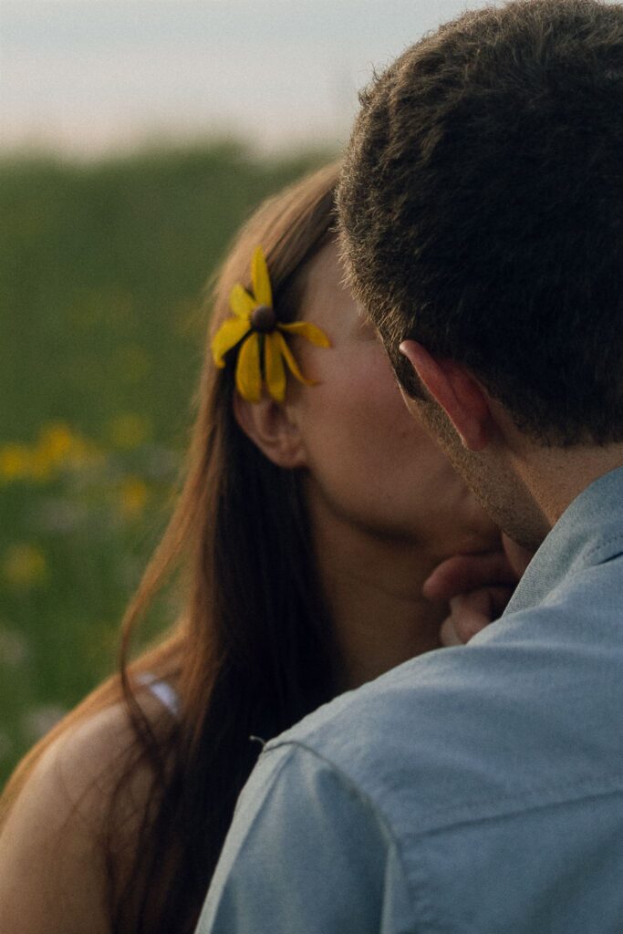 Close-up of Sophie and Jake kissing, her yellow flower brushing softly against his cheek — tender and cinematic.