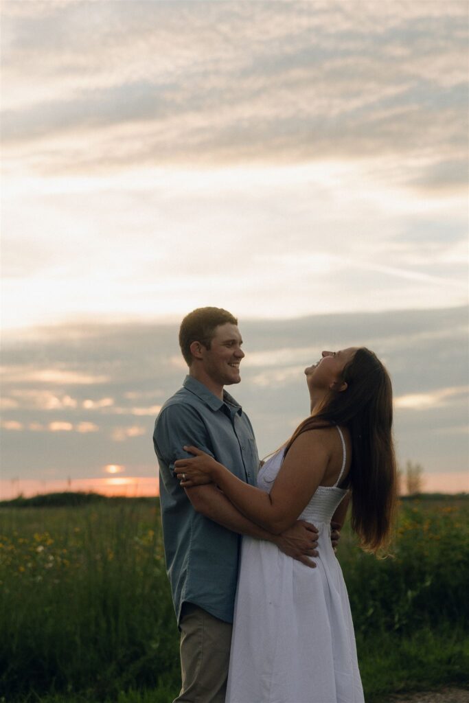 Sophie and Jake laughing together as the sun sets behind them, holding each other in the glow of golden hour in storytelling engagement photos.