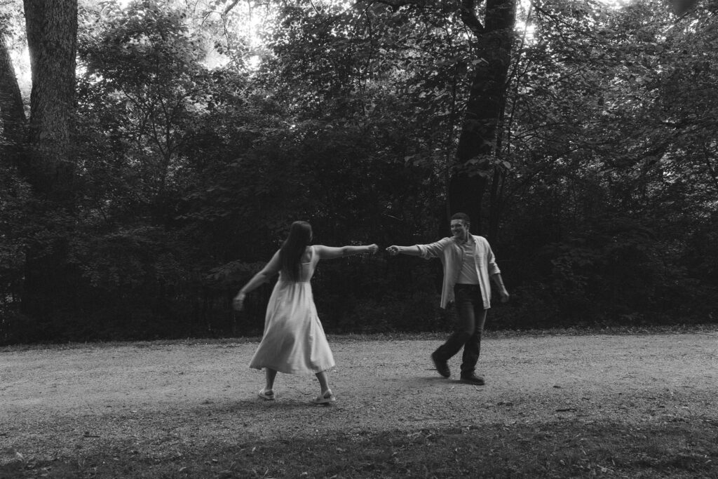 Black and white photo of the couple dancing under a canopy of trees, spinning each other around mid-laughter for their storytelling engagement photos.