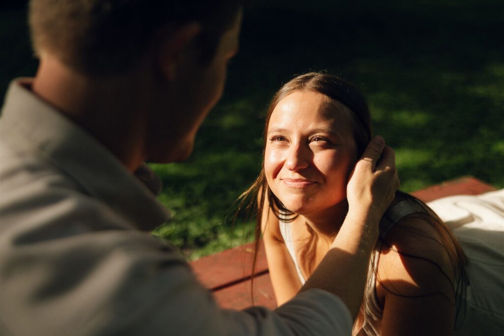 Close-up of Sophie smiling up at Jake as sunlight hits her face, candid and full of warmth in storytelling engagement photos.