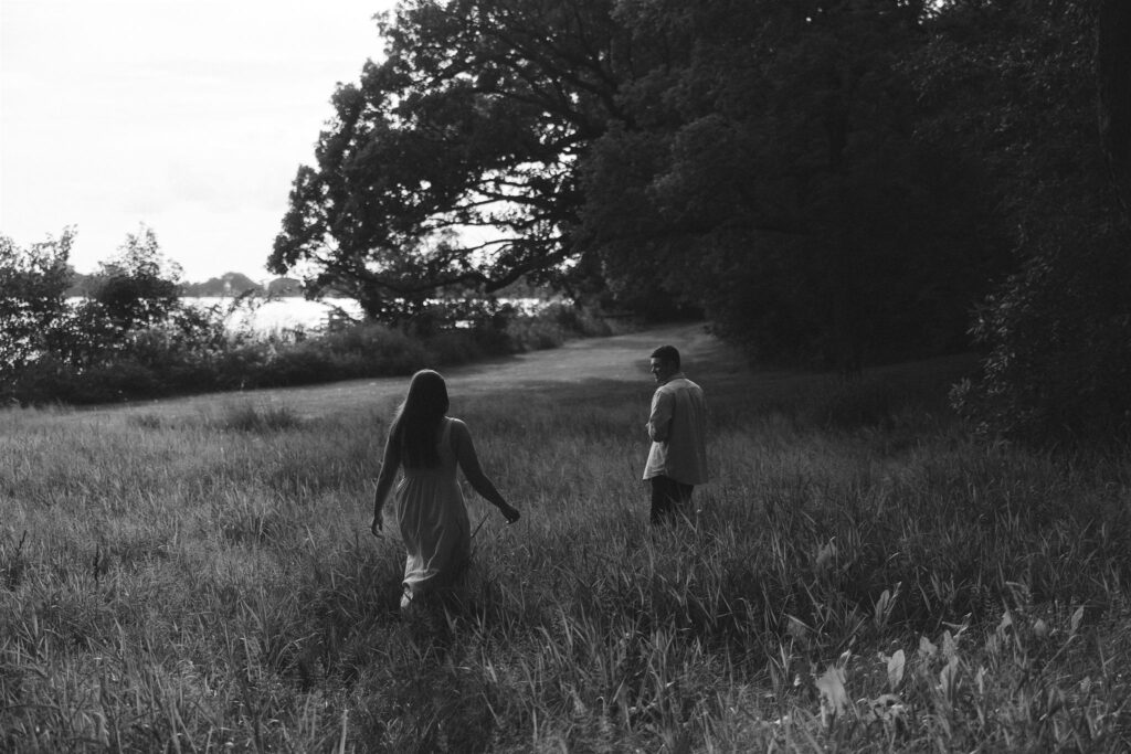 Couple walking through meadow of tall grass in Minnesota storytelling engagement photos.