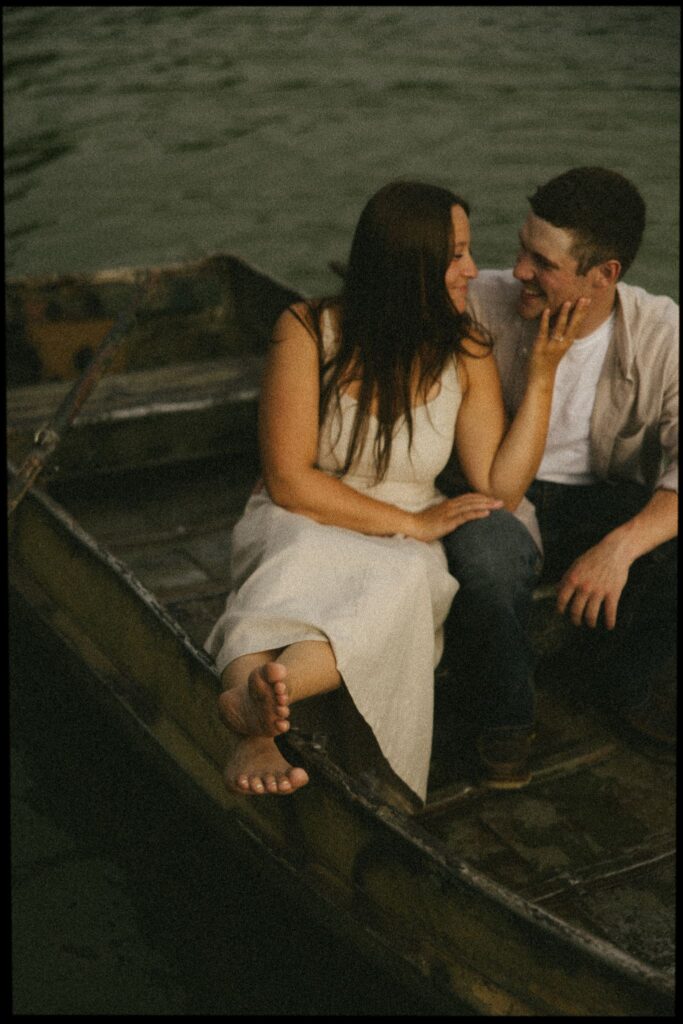 Close-up of Sophie sitting barefoot in the boat, hand on Jake’s cheek, the two of them laughing mid-conversation.