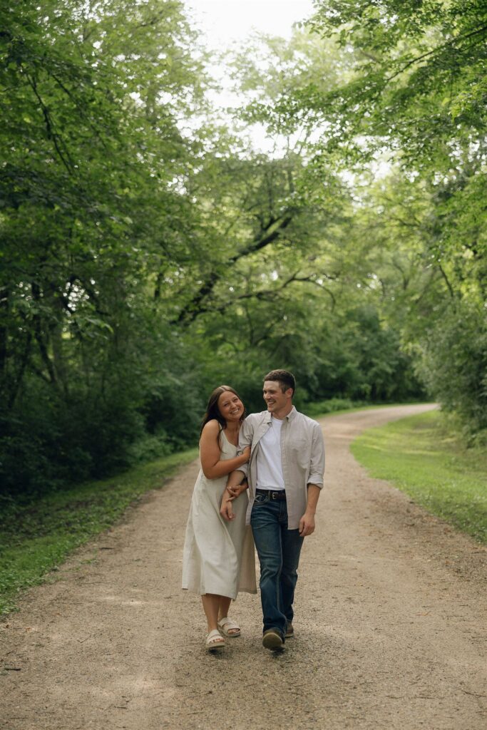 Sophie and Jake laughing together mid-walk, framed by winding woodland paths and warm light — the definition of easy, real love.