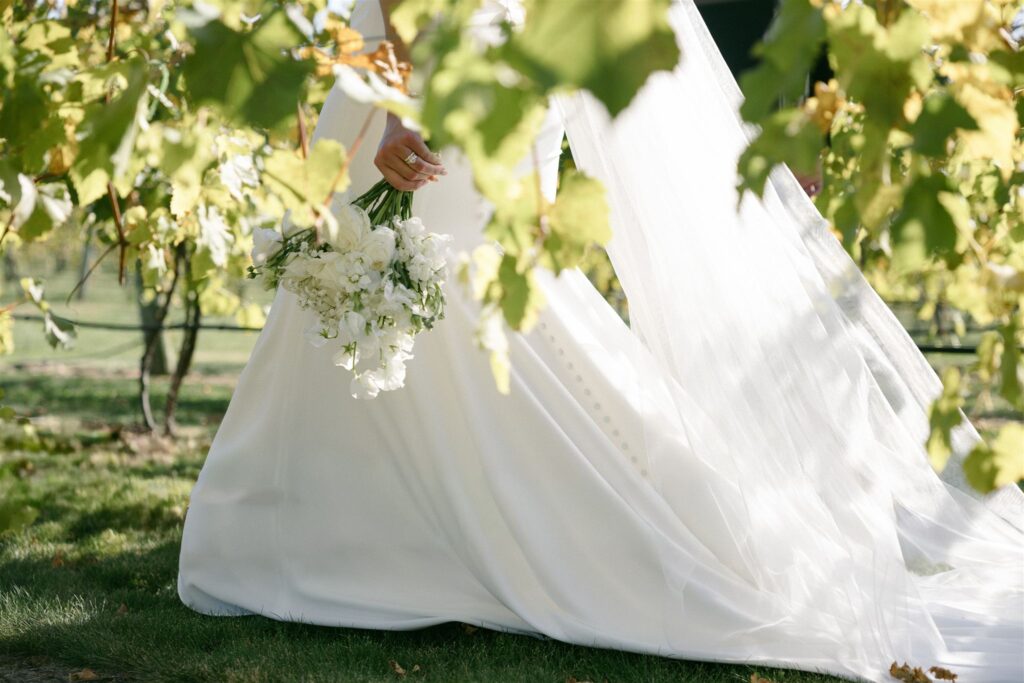 Close-up of bride’s white dress and bouquet photographed among vineyard leaves at 7 Vines Vineyard and Winery, highlighting texture and movement at one of the best wedding venues in Minnesota.
