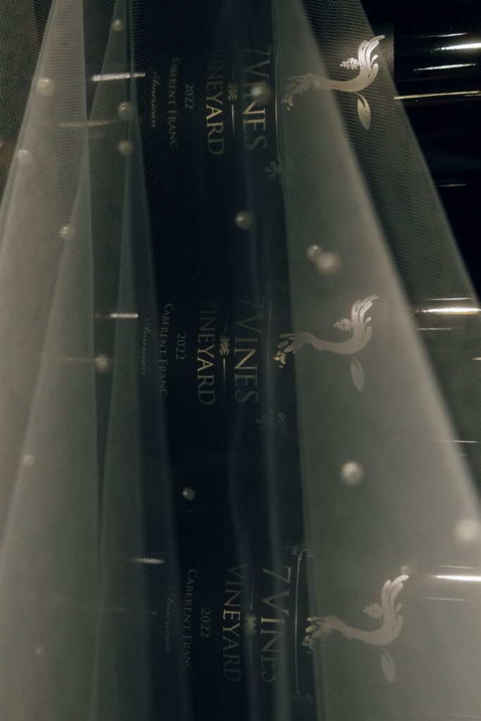 Close-up of wine bottles labeled “7 Vines Vineyard” photographed through a bridal veil, highlighting vineyard details at a Minnesota wedding venue.