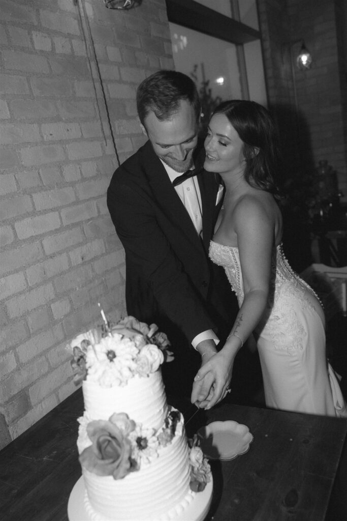Black-and-white image of bride and groom cutting their wedding cake together at an intimate Minnesota reception, a candid moment often recommended by experienced Minnesota wedding planners.