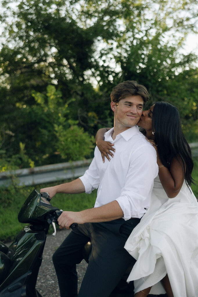 Amira leaning over Jake on the moped as he smiles, an editorial-leaning engagement photo that fits naturally among classic engagement photos in Minneapolis.