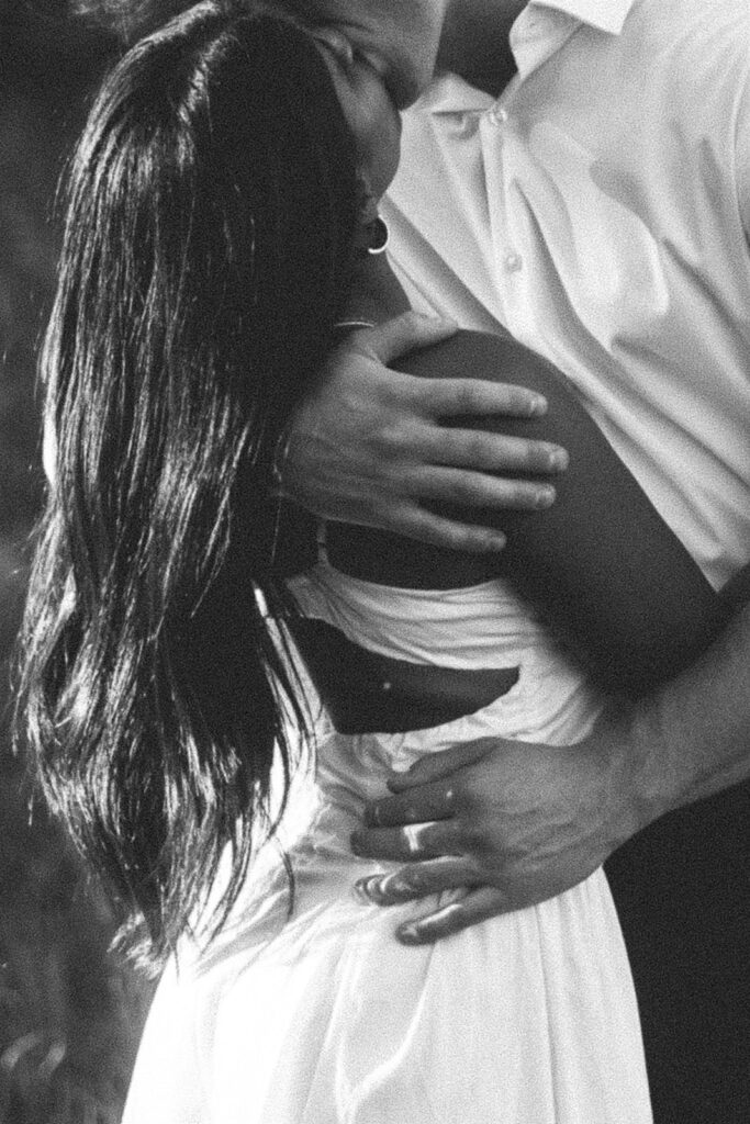 Black and white detail shot of Jake’s hand resting on Amira’s back, highlighting quiet connection and body language during their engagement photos.