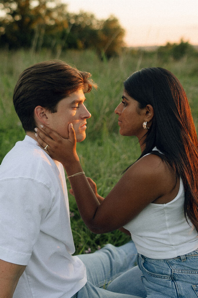 Jake and Amira sitting in tall grass, facing each other closely as Amira cradles his face, golden hour light softening the scene.