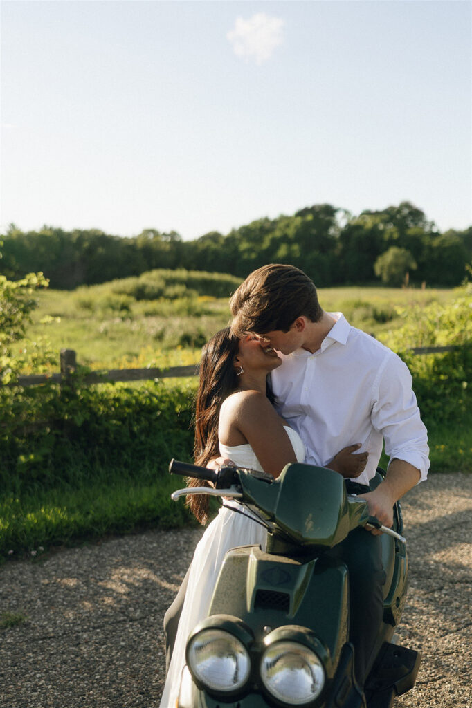 Close, intimate engagement photo of Amira and Jake kissing on the moped in an open field, blending classic engagement photos with modern ease.
