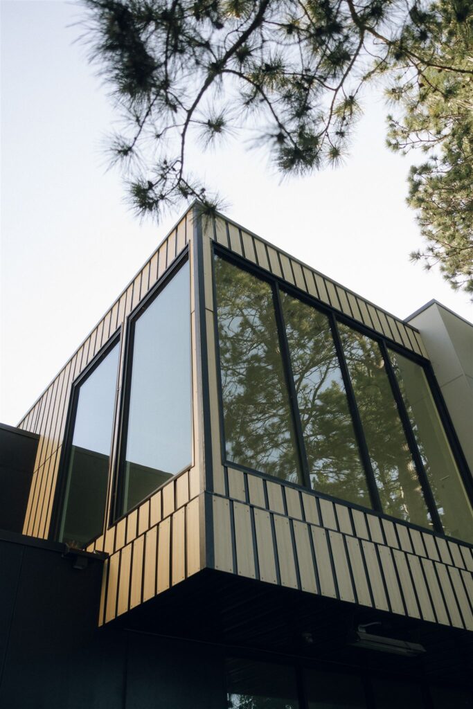 Exterior architectural detail of Catalyst by Nature Link featuring a modern corner with vertical wood siding and large black-framed windows, surrounded by pine trees at this contemporary Minnesota wedding venue.