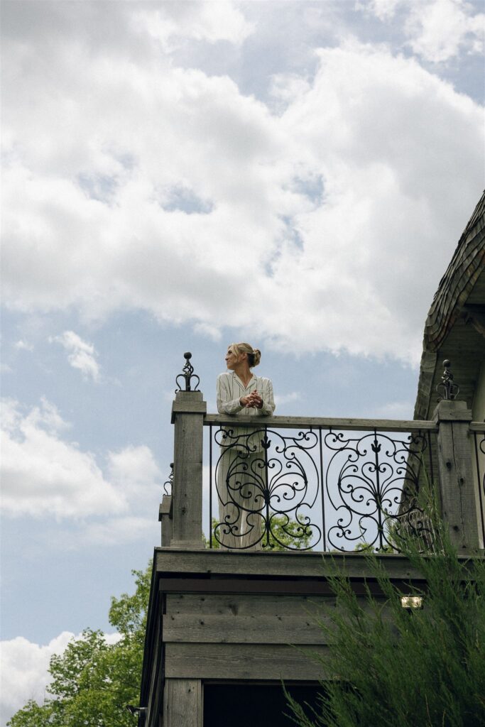 Bride stands on an iron-railed balcony at Edward Anne Estate, overlooking the grounds in a quiet pre-ceremony moment.