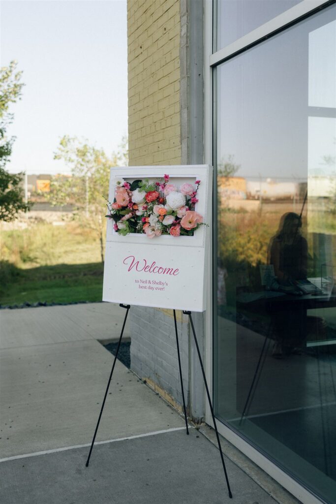 Wedding welcome sign on an easel outside the venue entrance, featuring floral details and greeting guests as they arrive.