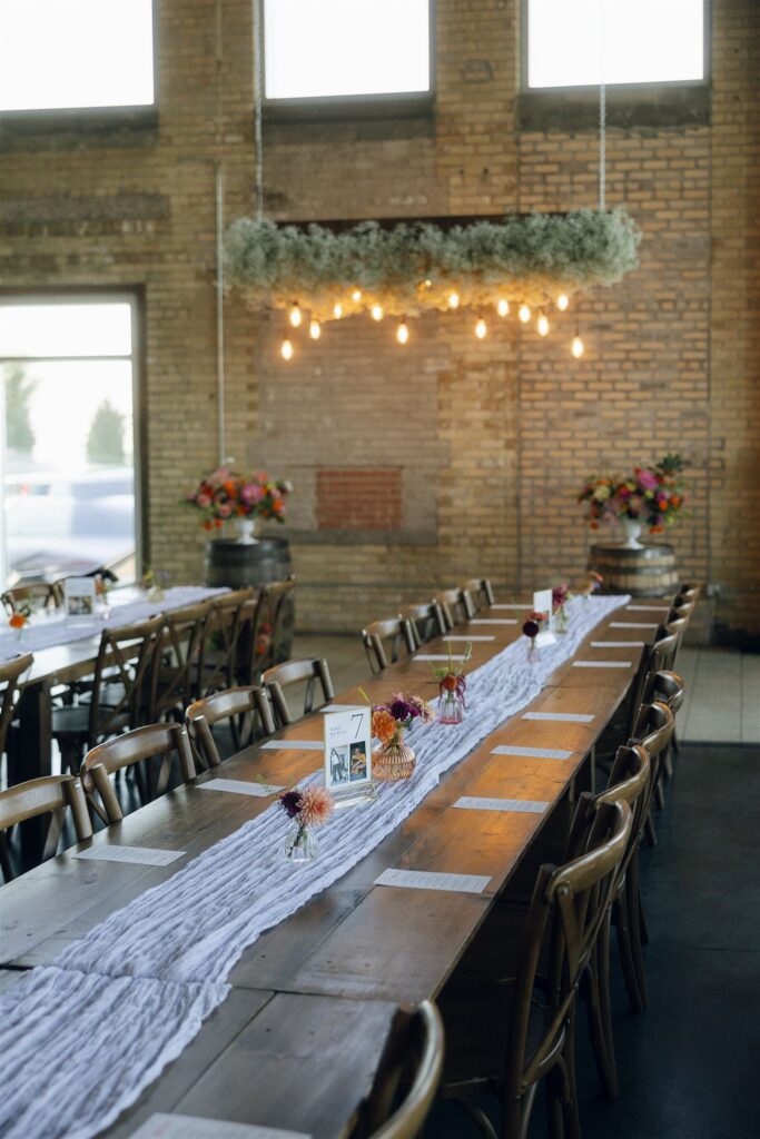 Long wooden reception tables styled with runners, bud vases, and candles inside a brick venue, a layout often recommended by Minnesota wedding planners.