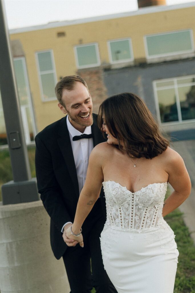 Bride and groom laughing together outside their venue, capturing a candid newlywed moment with soft, natural light and relaxed energy.
