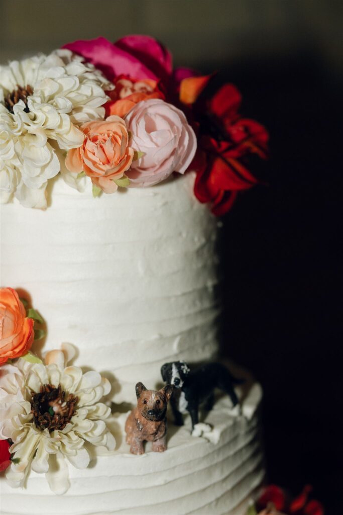 Detail photo of a white wedding cake decorated with bold florals and miniature dog figurines, reflecting playful, non-traditional wedding planning resources.