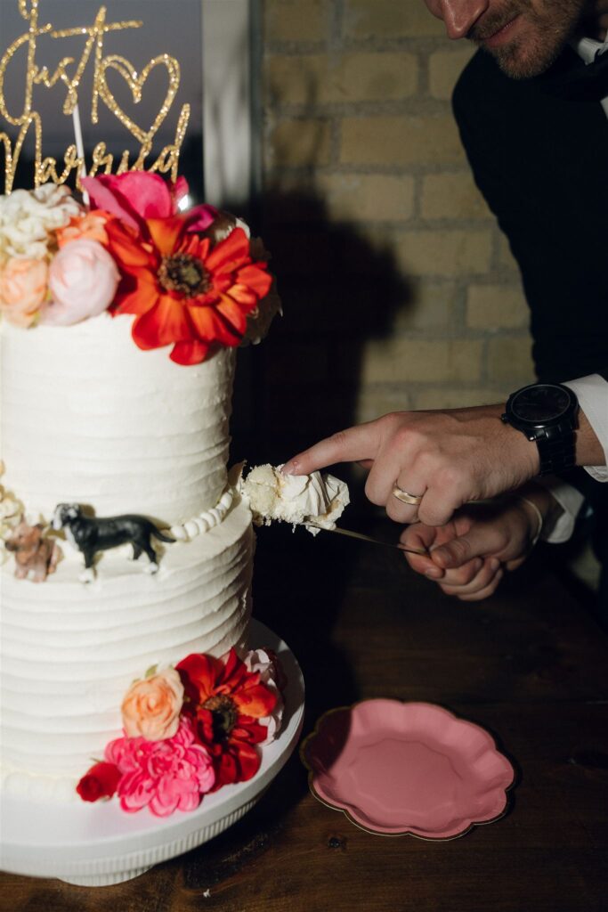 Groom cutting wedding cake with floral accents and custom cake toppers, featuring vibrant tones aligned with wedding colors 2026.