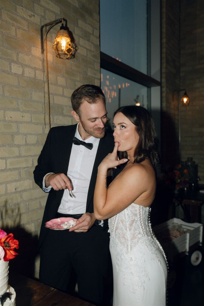 Bride tasting cake playfully while the groom looks on during the reception, a candid moment often captured by Minnesota wedding planners and photographers.