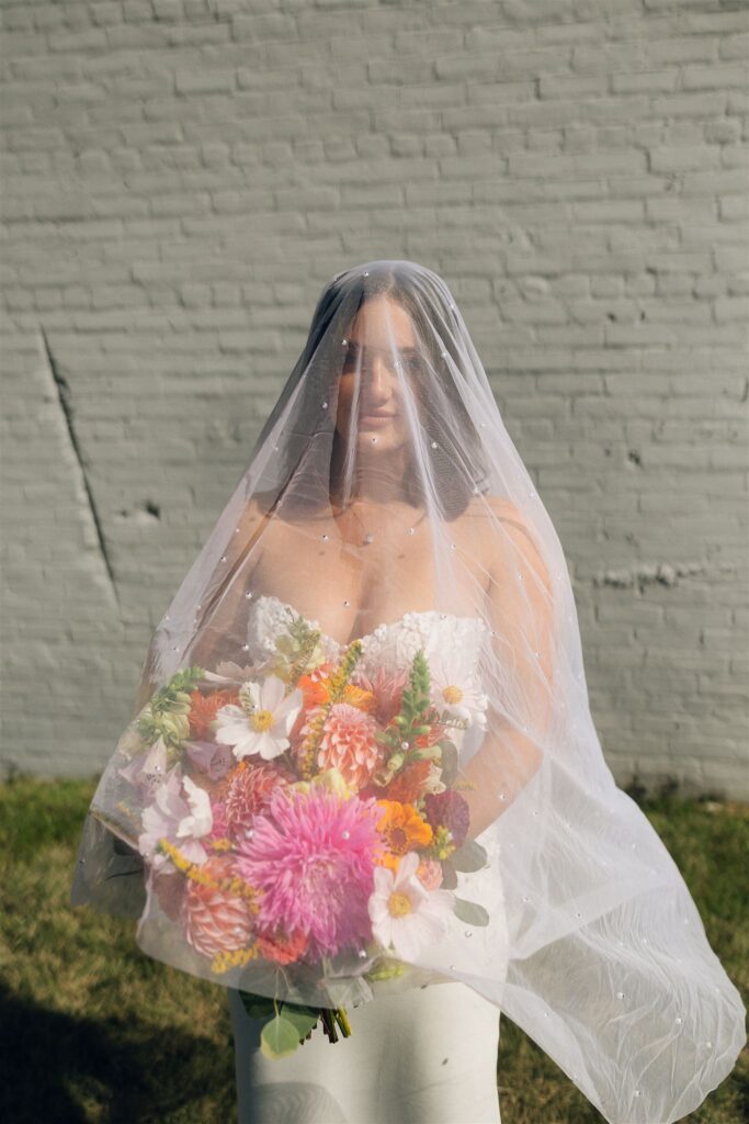 Bride standing outdoors holding a colorful wedding bouquet beneath a sheer veil, featuring vibrant florals that reflect wedding colors 2026 and modern Minnesota wedding planning style.