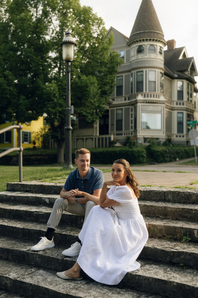 Couple running up the historic stone steps in St. Paul during their engagement session, her white dress catching the breeze as he chases after her in golden hour light.