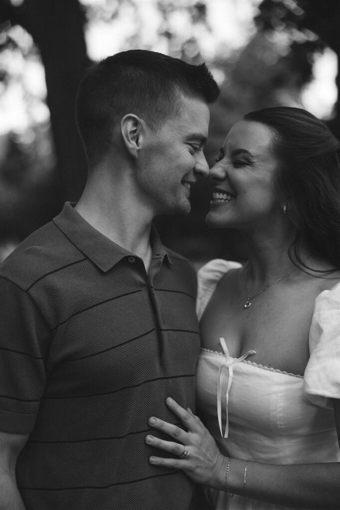 Close-up black and white engagement photo of a couple smiling nose-to-nose, her engagement ring visible as they lean into each other.
