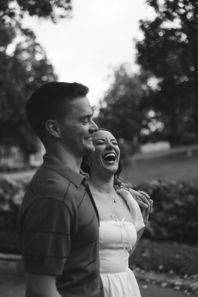 Black and white candid of an engaged couple laughing together beneath a vintage streetlamp during their St. Paul engagement photos.