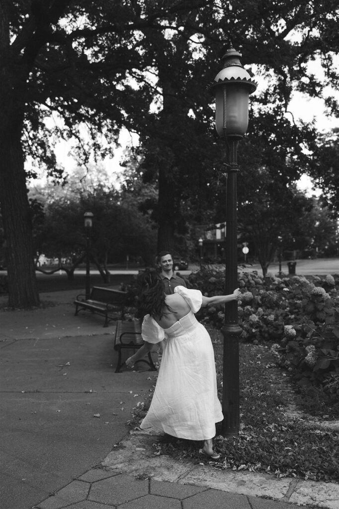 Black and white image of a couple playing around a historic streetlamp in St. Paul, blending romance with a little theatrical flair.