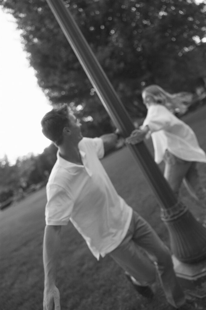 A blurred black and white shot of the two of them spinning around a lamppost, hands clasped and mid-laughter, motion caught in the edges of the frame.