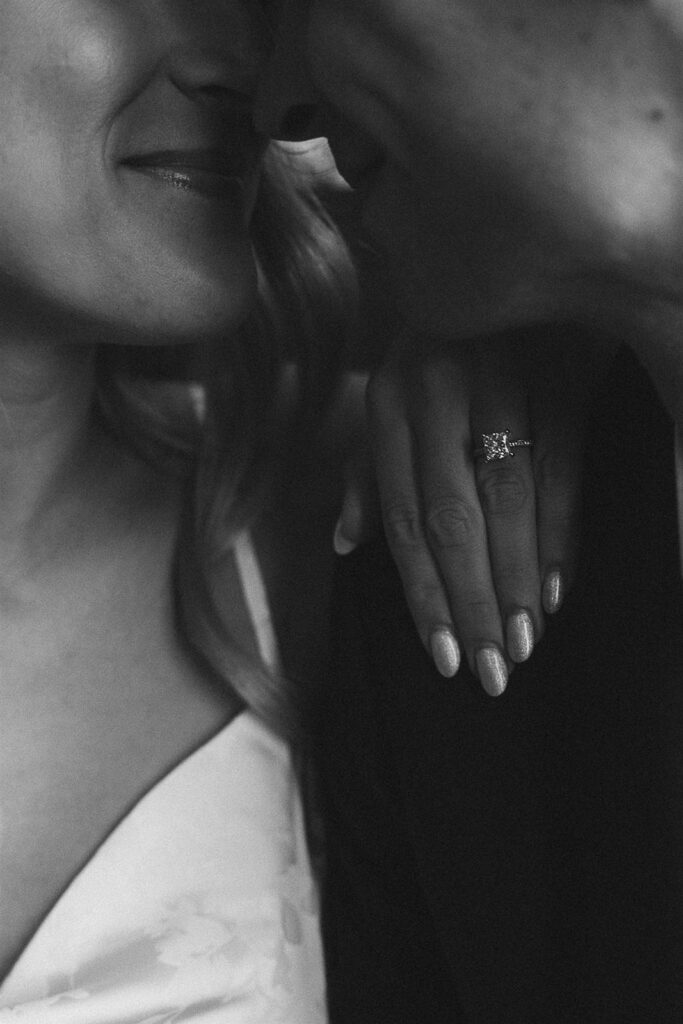 Artistic black and white close-up of a bride-to-be’s engagement ring as she leans into her fiancé, an intimate moment from their St. Paul engagement photos.