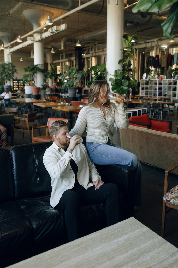 She perches on his lap in the brewery lounge, both of them laughing — engagement photos unique because they’re not trying to be anything else.