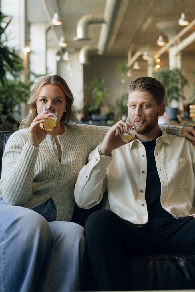 The two of them shoulder-to-shoulder on a leather couch, drinks in hand, relaxed and fully themselves during their Minneapolis engagement session.