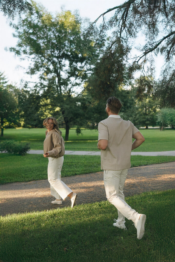 The couple walking through a sunny Minneapolis park, mid-conversation, mid-laugh, not looking at the camera once.