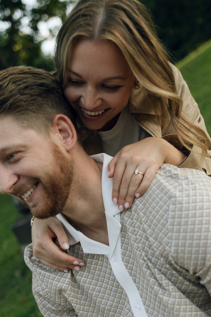 Close-up of her grinning as she climbs onto his back for a piggyback ride — playful engagement photos that feel lived-in.