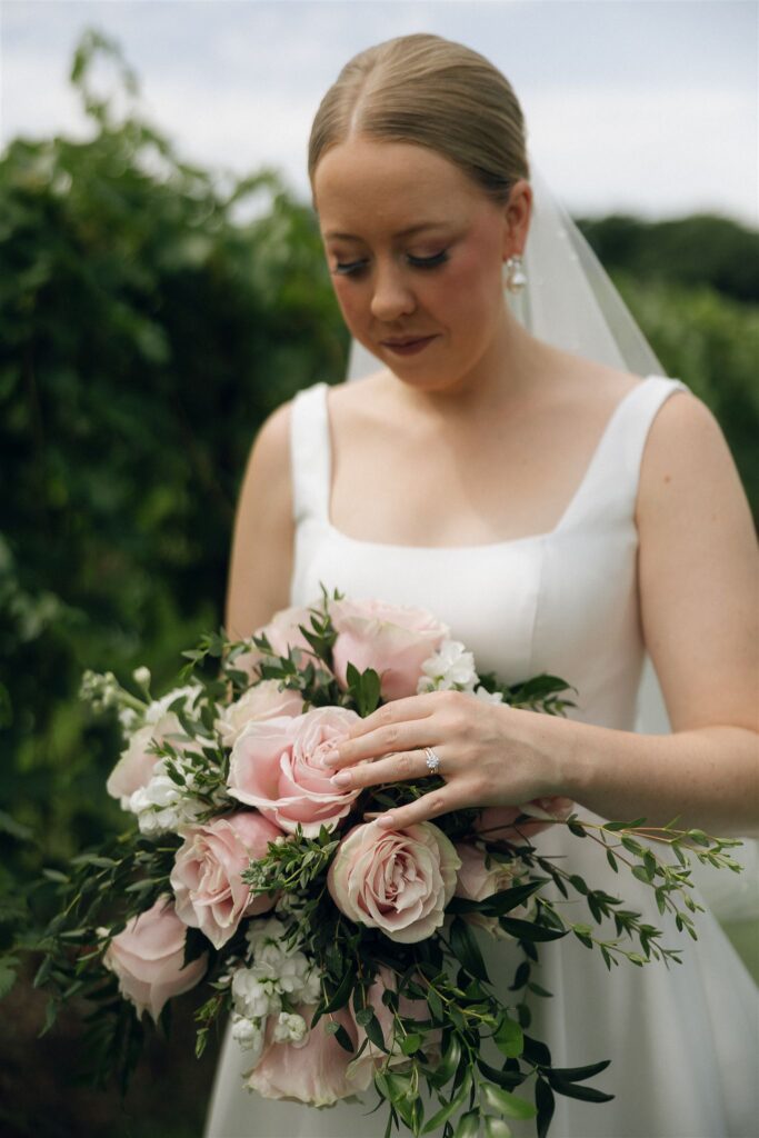 Bride walking through vineyard lawn with groom holding her train, summer greenery surrounding them at 7 Vines Vineyard and Winery.