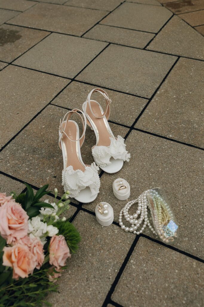 Wedding detail flat lay with pearl heels, rings, blush bouquet, and beaded clutch on patio at 7 Vines Vineyard and Winery.
