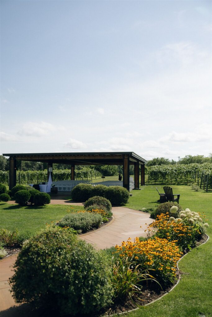 Outdoor ceremony setup at 7 Vines Vineyard and Winery with vineyard rows stretching behind the covered pavilion on a sunny August afternoon.