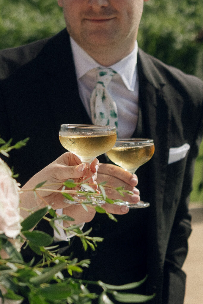 Bride and groom clinking coupe glasses filled with champagne at 7 Vines Vineyard and Winery, celebrating with the vineyard rows behind them.