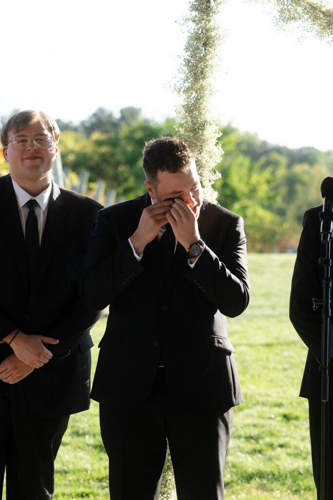 Groom reacting emotionally during ceremony as guests smile and watch.