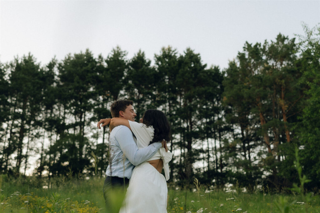 Engagement photo of a couple hugging tightly in a grassy field, arms wrapped fully around each other, capturing physical touch as the central storytelling element.