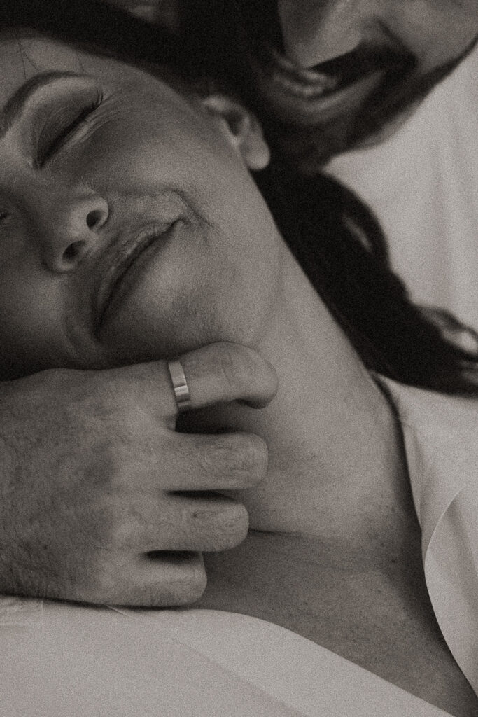 Black and white close-up of a couple resting together, his hand gently holding her jaw as she smiles with her eyes closed during an intimate engagement session