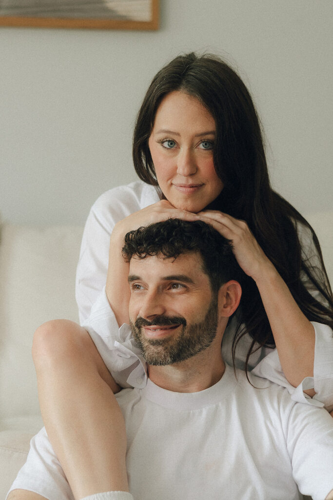 Casual engagement portrait of a couple sitting on the floor in front of the couch, her leg draped over his shoulder while he leans into her effortlessly