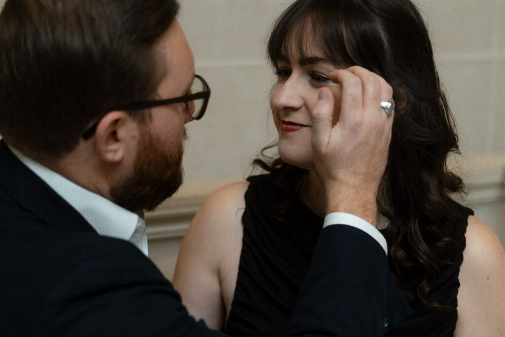 Close-up of a man in a suit gently brushing hair away from a woman’s face as she smiles at him.