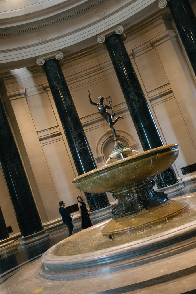 Ornate museum fountain with bronze statue centered beneath a domed ceiling and surrounding columns.