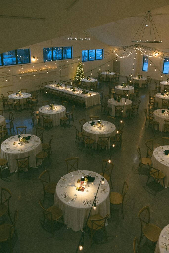 Overhead view of a wedding reception space lit with string lights and candlelight, showcasing ambient wedding lighting photography with round tables, warm tones, and a softly glowing atmosphere.