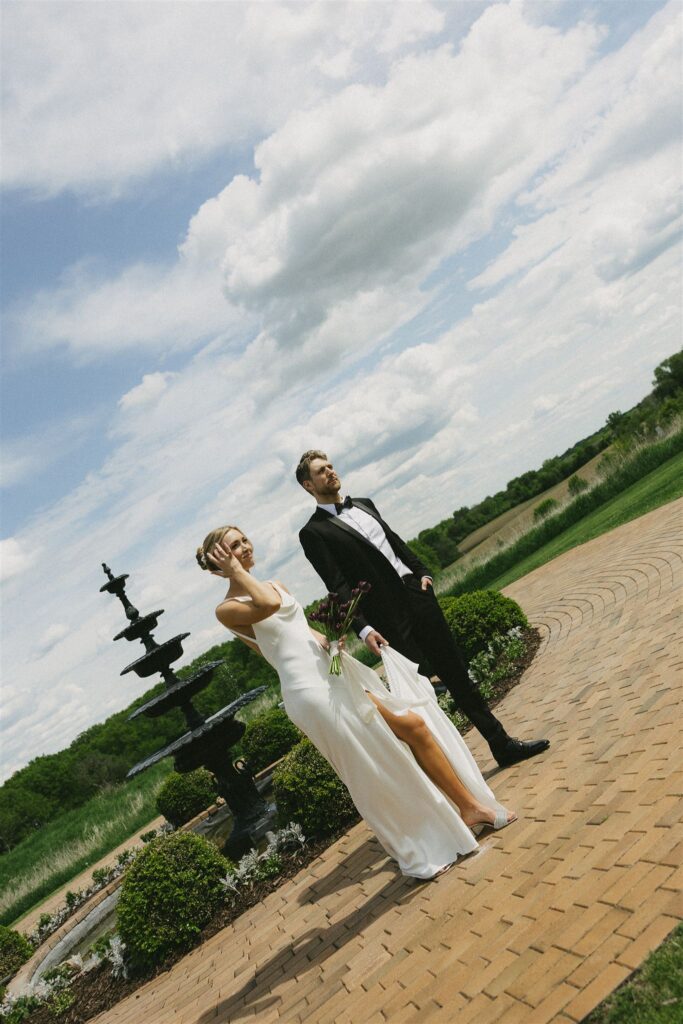 Bride and groom standing near a fountain under an overcast sky, evenly lit with soft shadows as clouds diffuse the light, illustrating how overcast conditions create calm, balanced tones in wedding lighting photography.