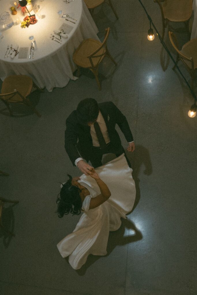 Top-down view of a couple dancing during their wedding reception, photographed using ambient lighting with overhead string lights and candlelight creating a moody, intimate feel.