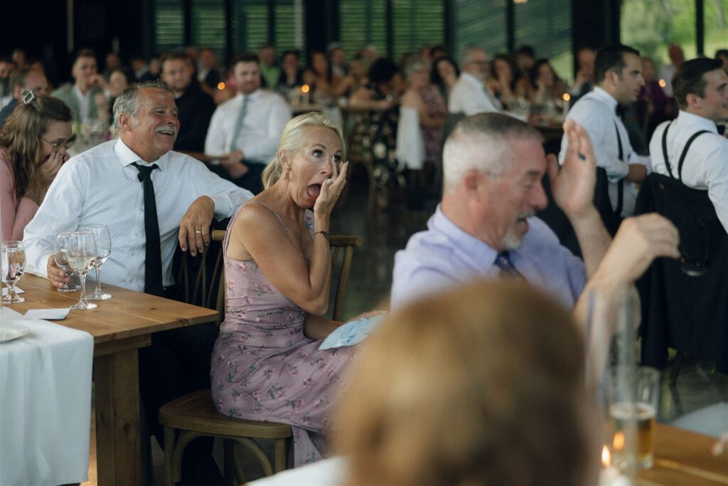Wedding guest reacts emotionally during reception speeches, photographed in ambient candlelight and venue lighting that preserves the natural mood of the room.
