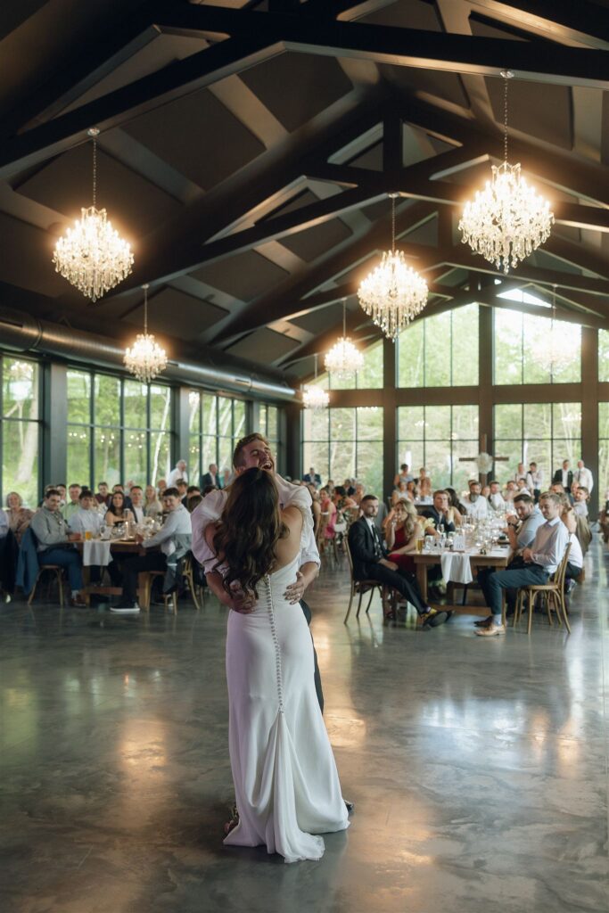 Wide shot of a couple dancing under chandeliers at their wedding reception, showcasing ambient wedding lighting photography that highlights the scale, warmth, and atmosphere of the venue.